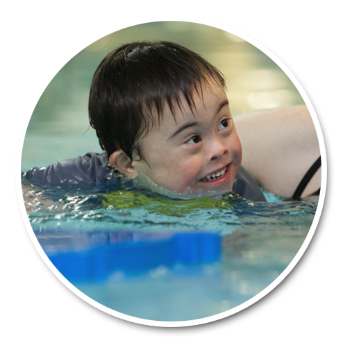 An instructor supporting a smiling child with a disability during an adapted aquatics session