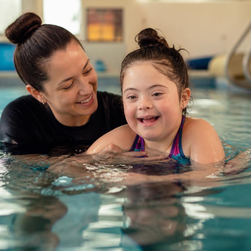 An instructor supporting a smiling child with a disability during an adapted aquatics session