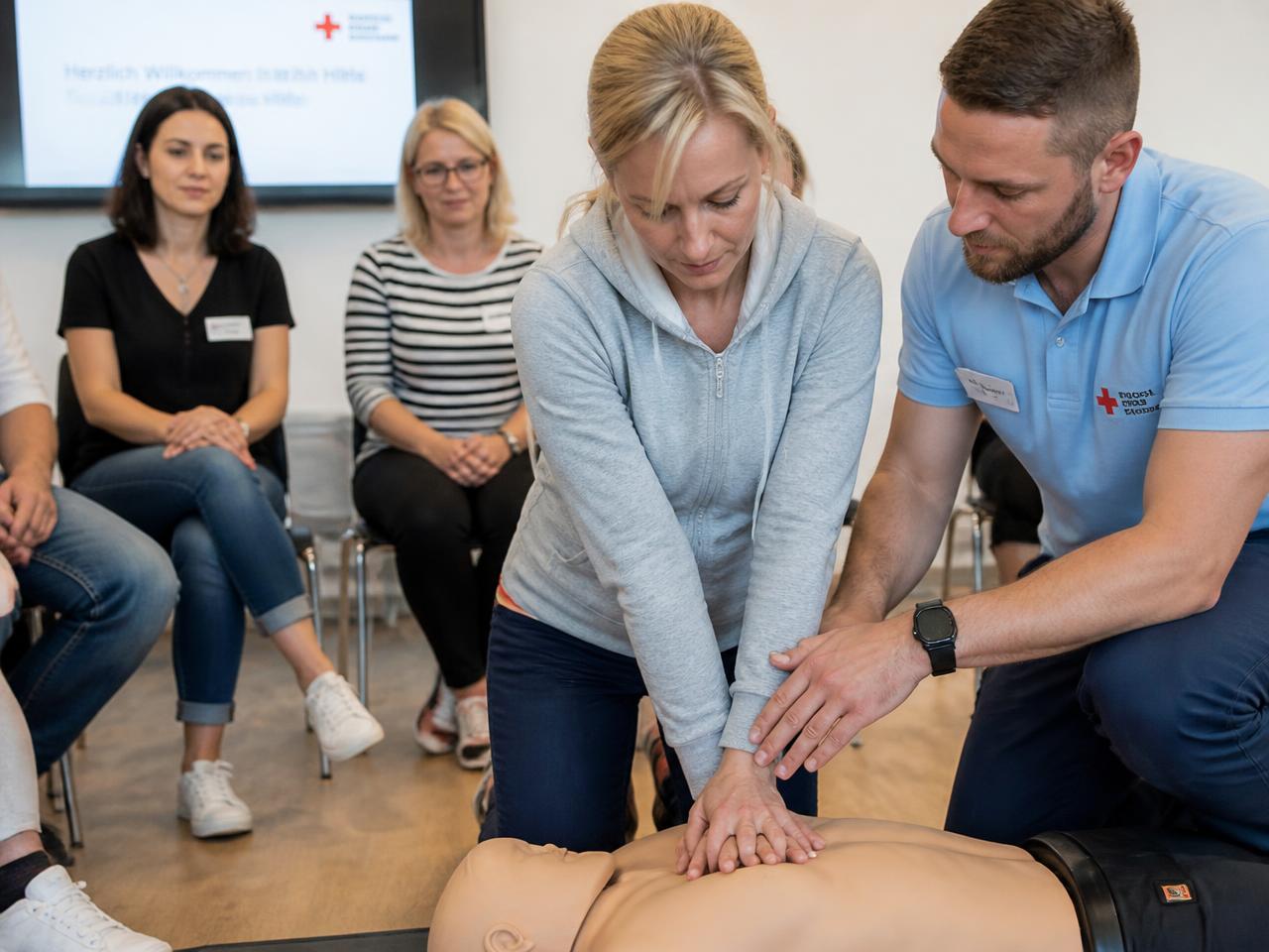 An instructor guiding a student practising chest compressions on a CPR training manikin