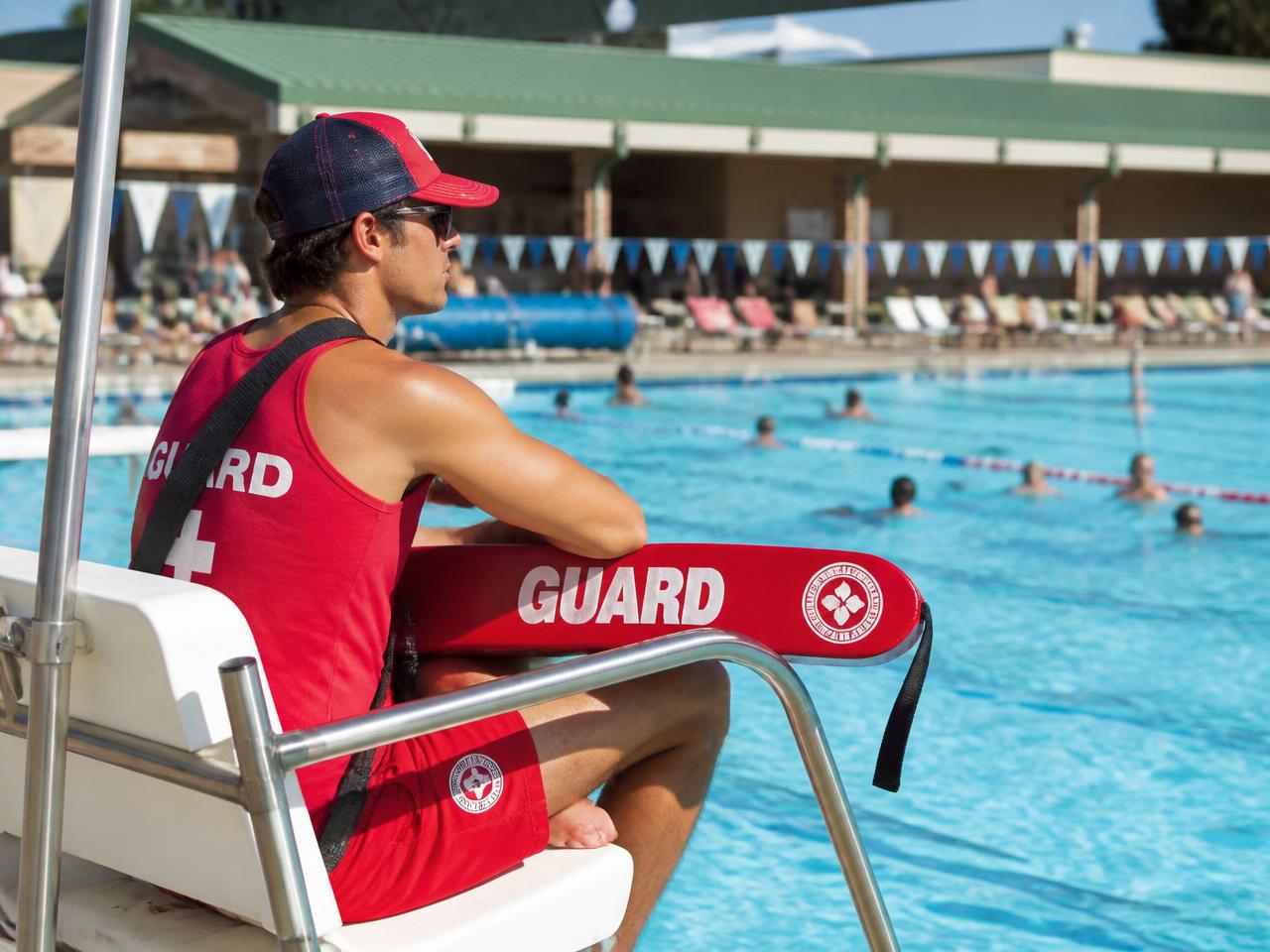 A lifeguard watching swimmers from a poolside station with a rescue tube